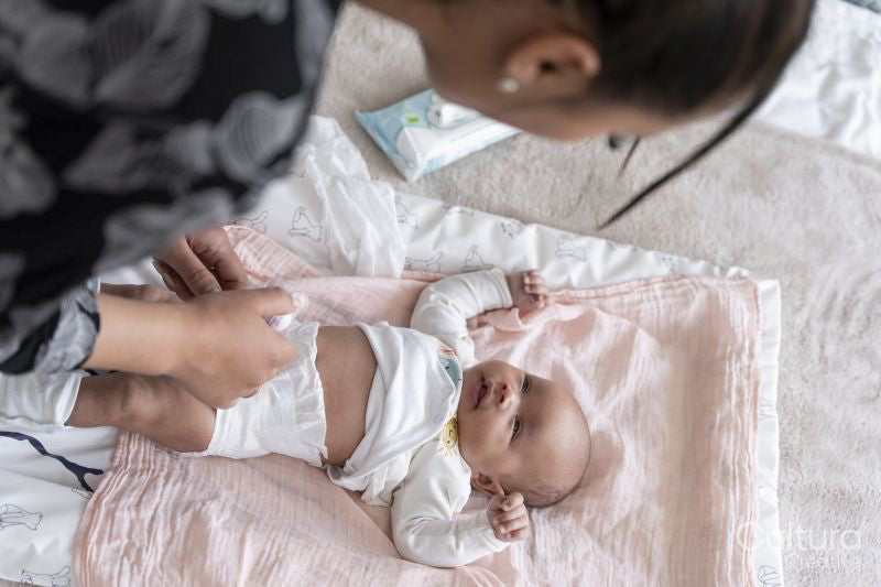 Mother changing diaper to newborn baby girl on bed at home