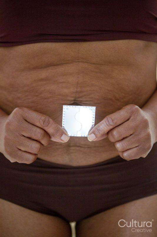 Mid section of woman holding hormone patch in front of belly