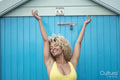 Smiling woman with arms up standing against blue wall