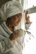 Woman in bathrobe and towel on head looking through window