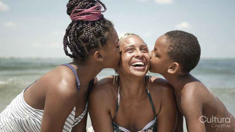Brother and sister kissing smiling mother on beach