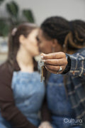 Two young women holding house key and kissing, focus on key in foreground
