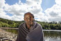 Smiling man wrapped in towel sitting on lakeshore, Yorkshire, UK
