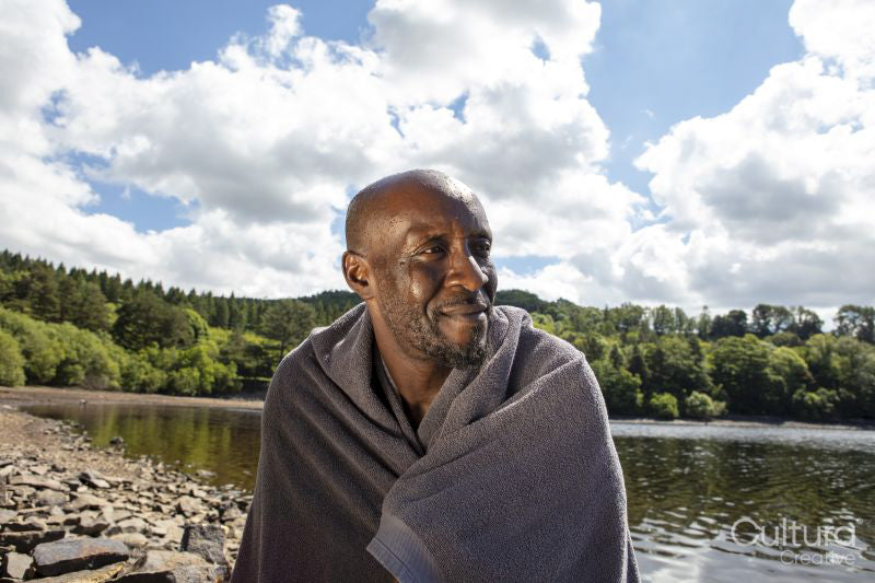 Smiling man wrapped in towel sitting on lakeshore, Yorkshire, UK