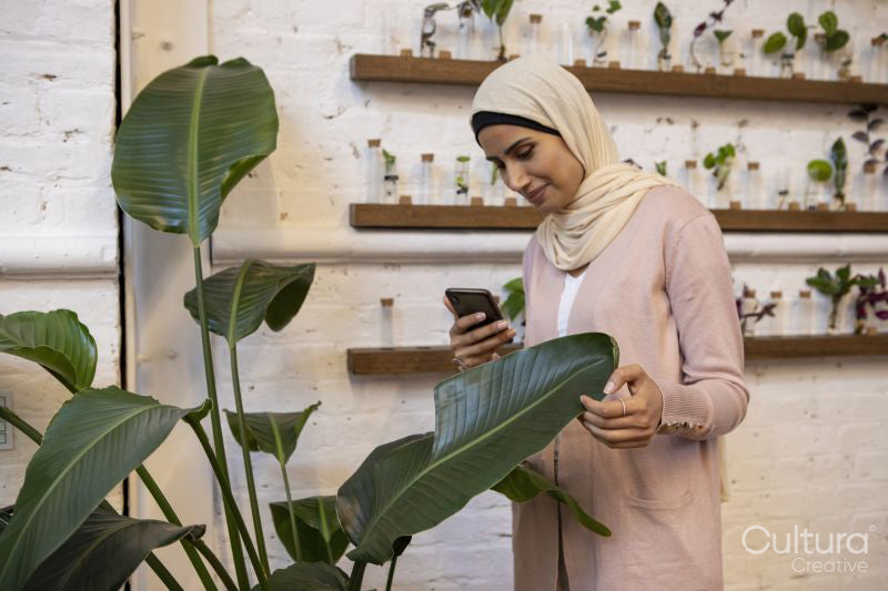 Woman wearing headscarf photographing banana leaf with smart phone