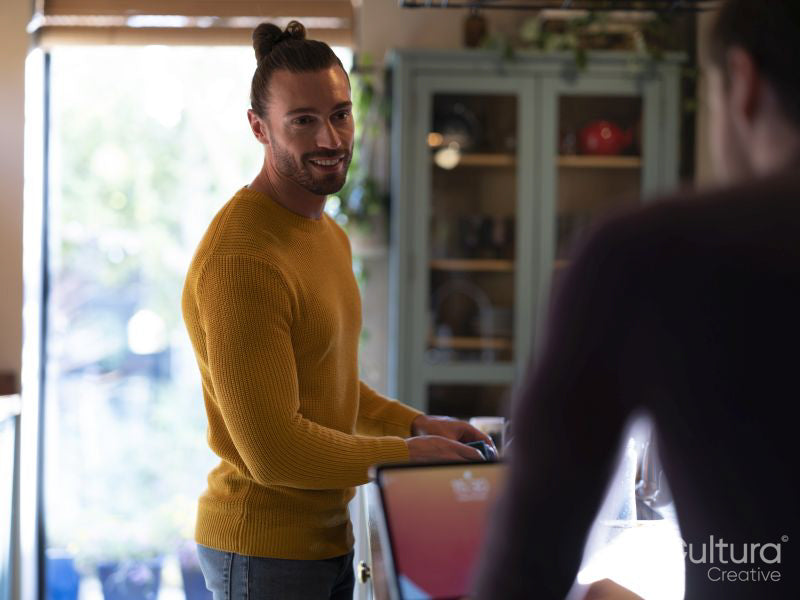 Man washing dishes while boyfriend using digital tablet at home kitchen