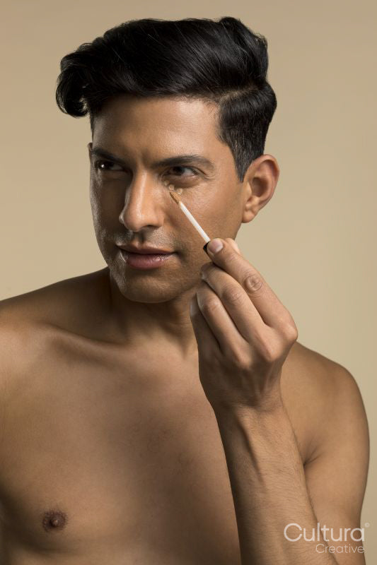 Studio portrait of shirtless man applying foundation under eye