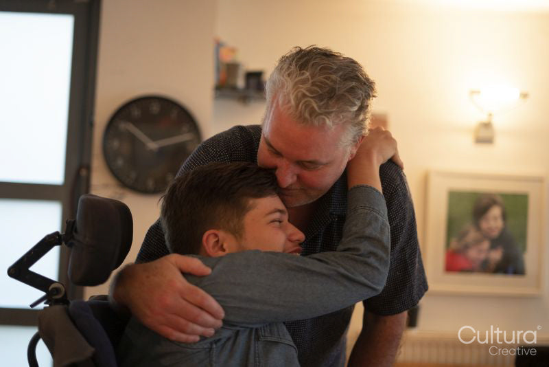 Father embracing disabled son at home