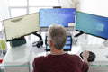 Mature man working on three monitors at home