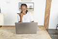 Young woman talking by phone while working on laptop at home