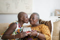 Smiling woman giving gift and kissing mother at home