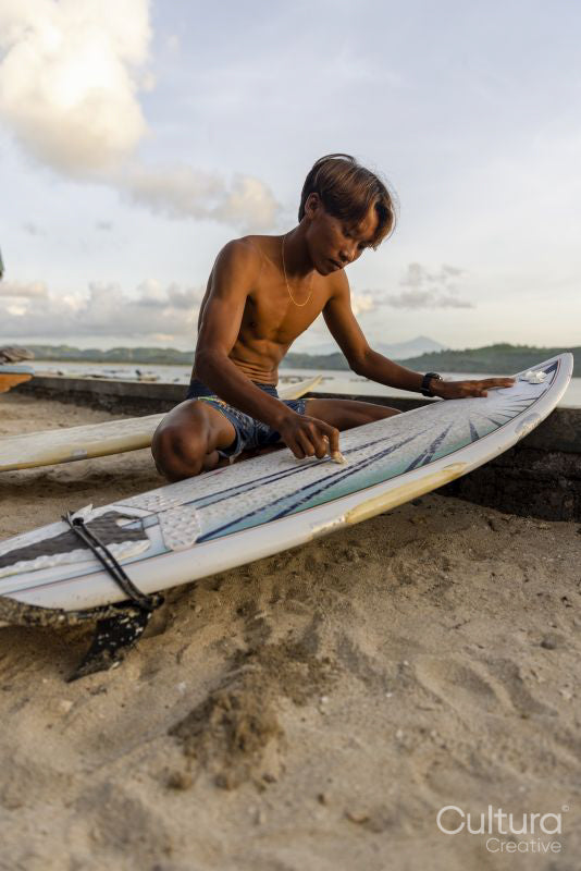 Surfer preparing surfboard on beach at sunset