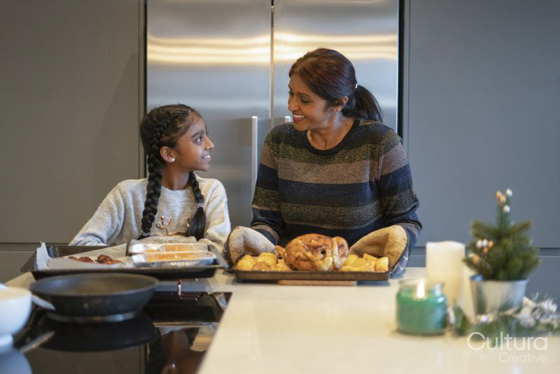 Smiling mother and daughter preparing roasted turkey in kitchen