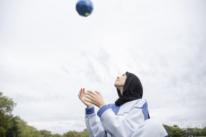 Woman in hijab sitting throwing soccer ball