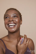 Studio portrait of smiling woman spraying perfume on neck