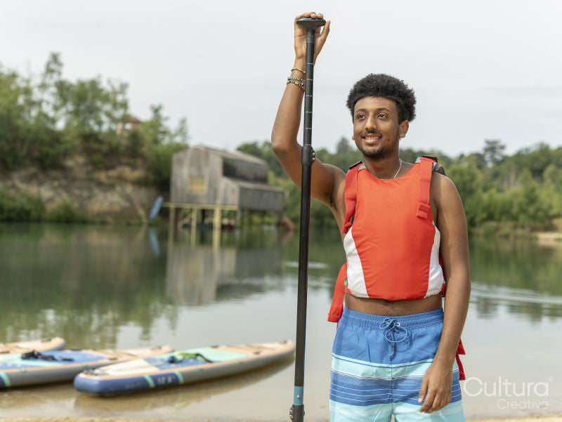 Portrait of young man standing with oar by lake