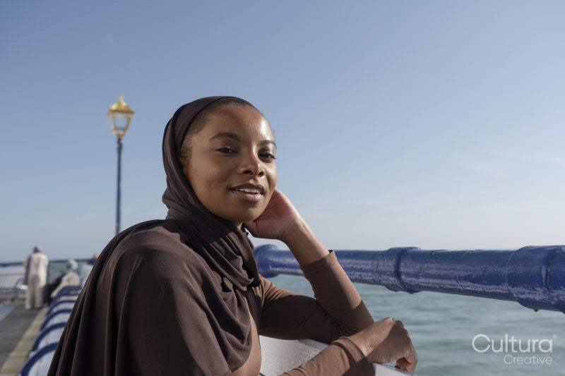 Portrait of Muslim woman looking at camera while leaning on railing by sea