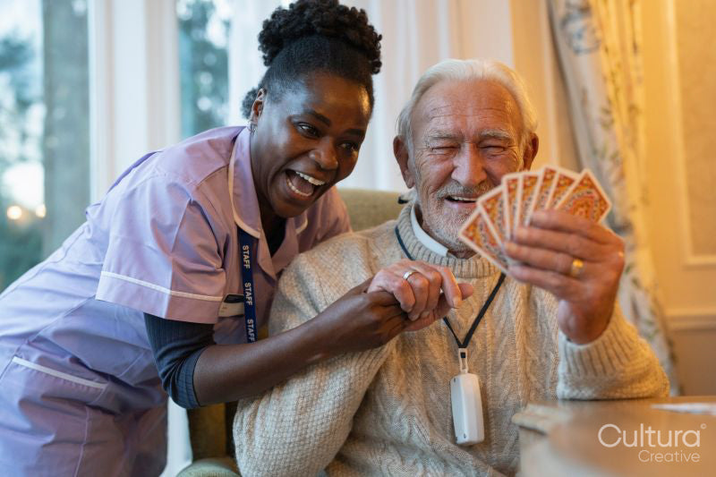 Smiling senior man and nurse playing cards at table in nursing home
