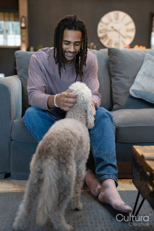 Man with dreads sitting on sofa and petting dog