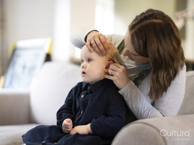 Mother adjusting daughters hearing aid at home