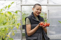 Portrait of smiling woman holding tomatoes in greenhouse