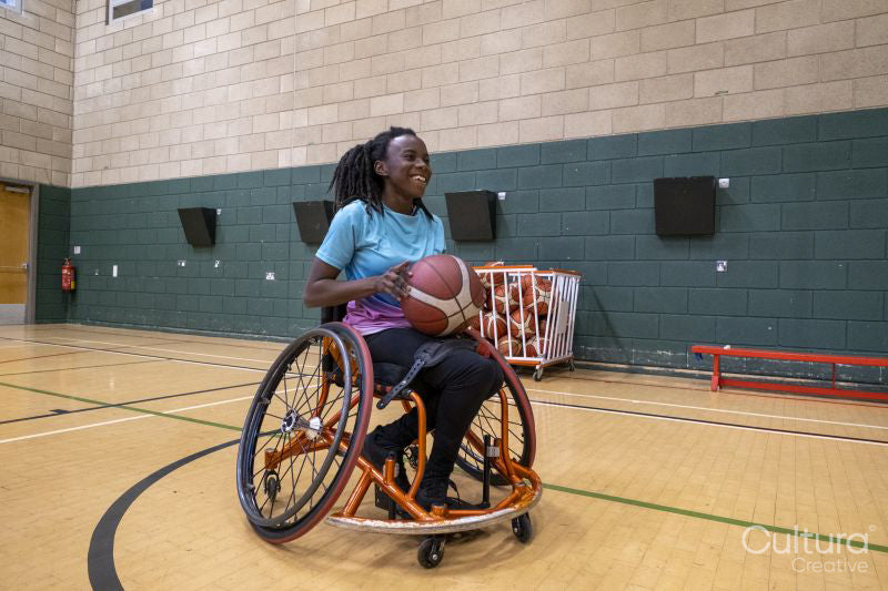 Teenage girl in wheelchair practicing basketball