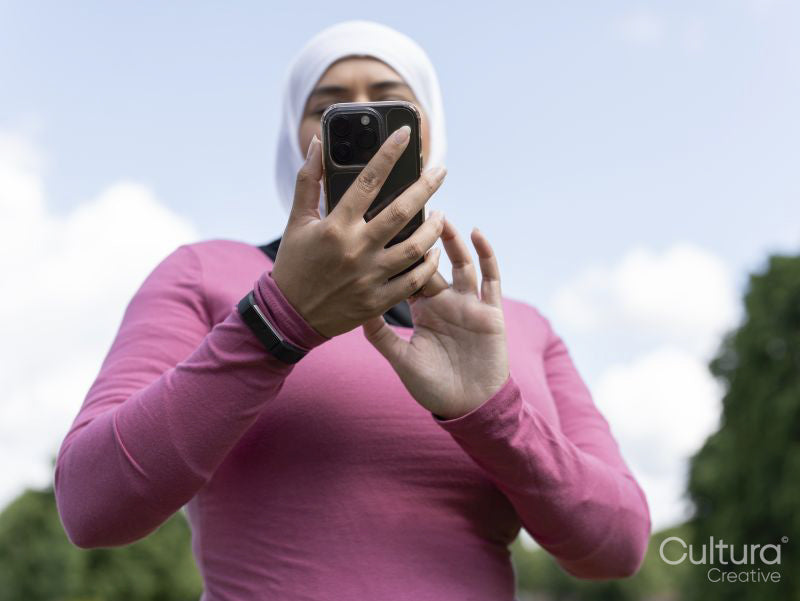 Sutton,Low angle view of woman in headscarf holding smart phone in park
