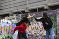 Laughing girl looking at friends piggybacking against graffiti wall