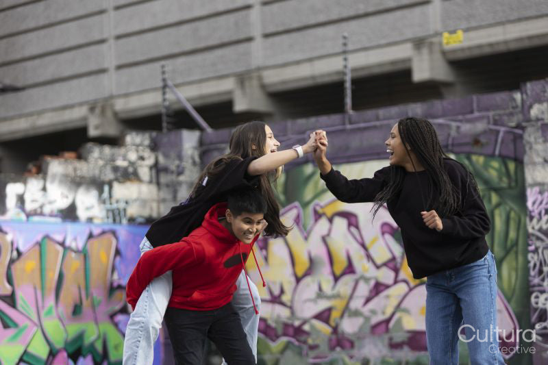 Laughing girl looking at friends piggybacking against graffiti wall