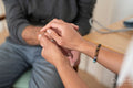 Close-up of female doctor and senior patient holding hands in office