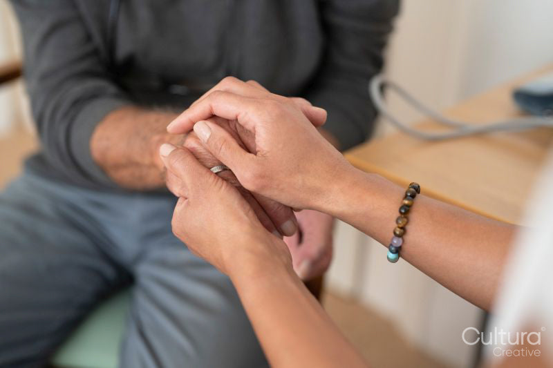 Close-up of female doctor and senior patient holding hands in office