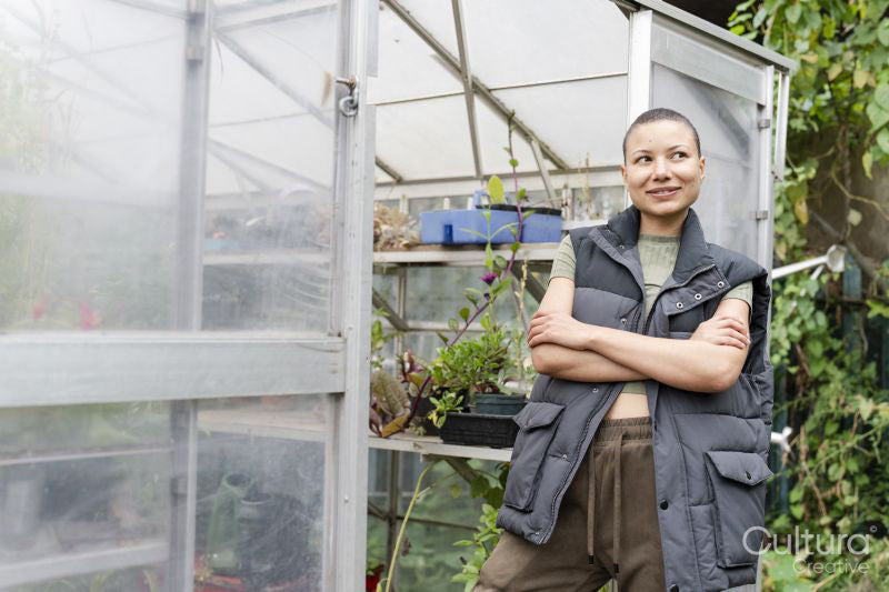 Portrait of smiling woman standing in front of greenhouse