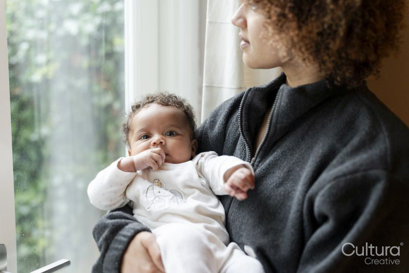 Mother holding baby daughter and looking out window