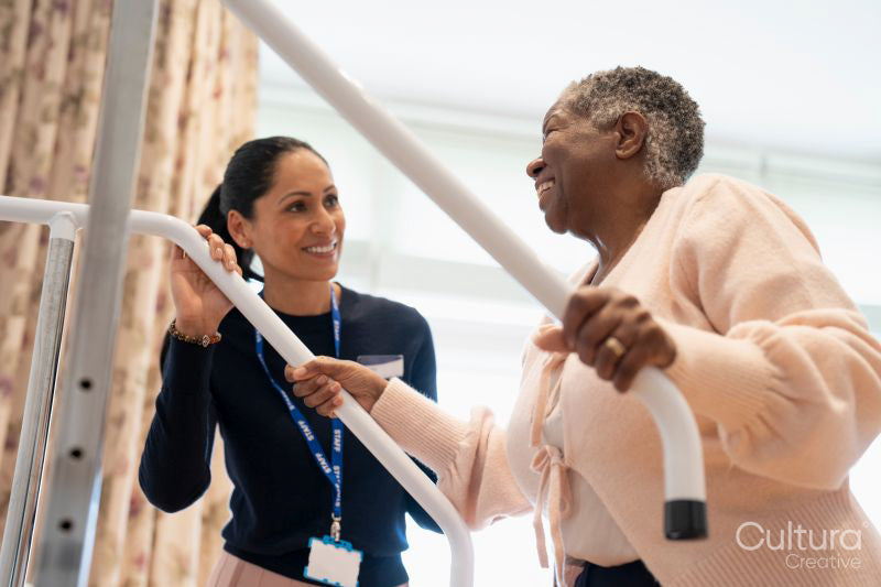 Smiling female therapist assisting senior woman ascending steps in exercise room