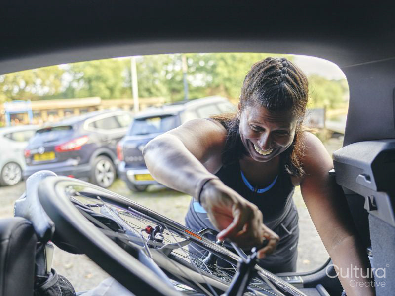Smiling sportswoman taking bicycle from back of car