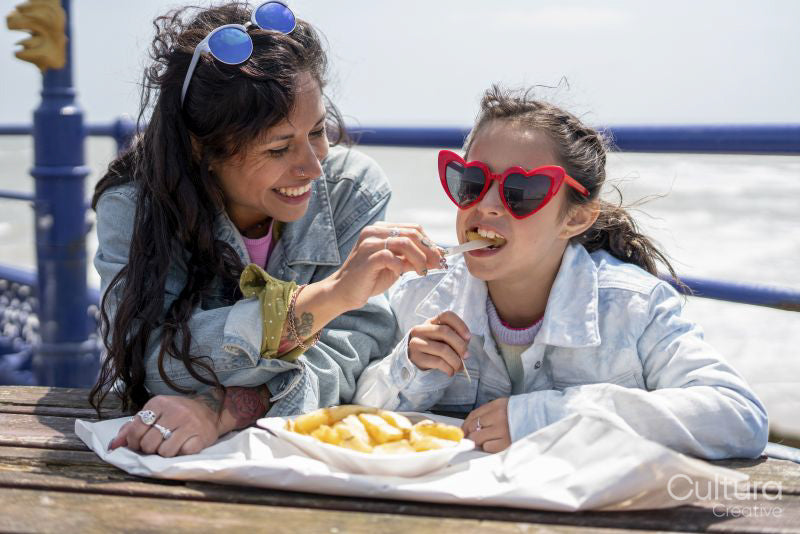 Mother and daughter eating fish and chips at seaside
