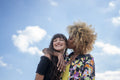 Woman giving girlfriend kiss on cheek against blue sky