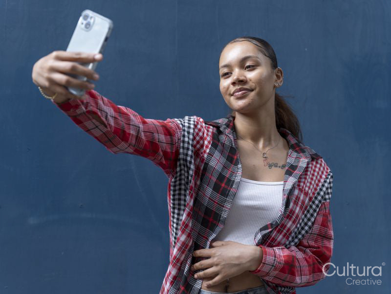 Young woman taking selfie against blue wall