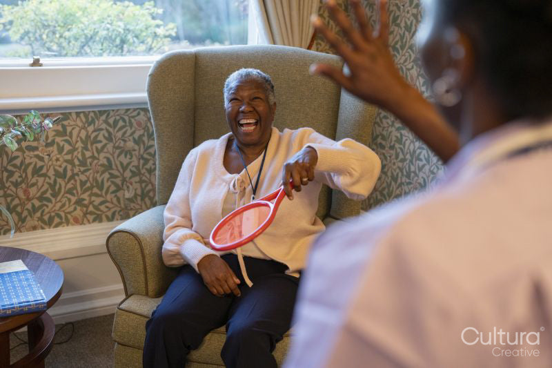 Smiling senior woman and nurse playing with balloon in nursing home