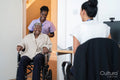 Smiling female nurse with senior woman sitting in wheelchair entering doctors office