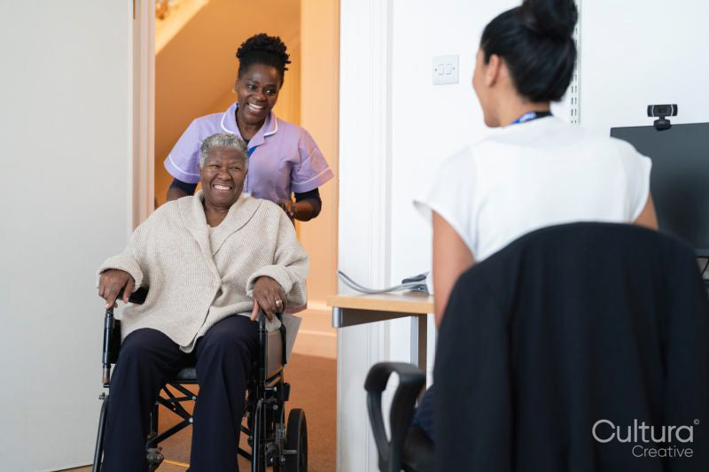 Smiling female nurse with senior woman sitting in wheelchair entering doctors office
