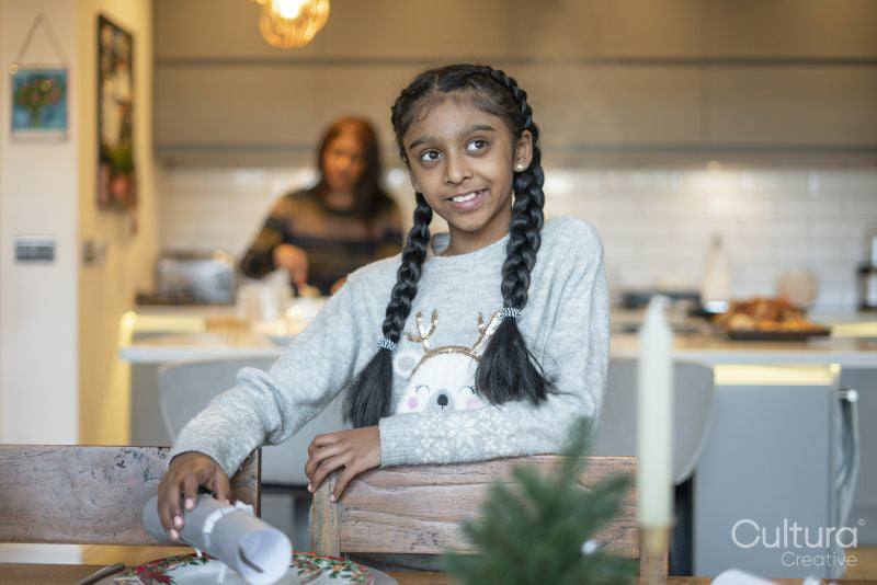 Smiling girl placing Christmas cracker on table, mother in background