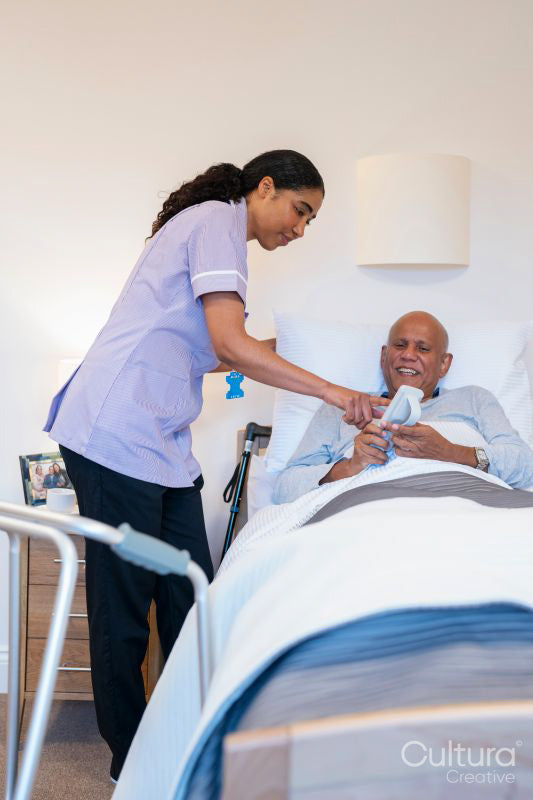 Nurse helping with remote control to senior man lying in adjustable bed in room at nursing home