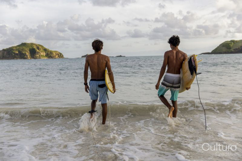 Indonesia, Lombok, Rear view of two surfers walking into sea