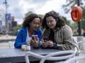 Smiling couple looking at smart phones at sidewalk cafe table