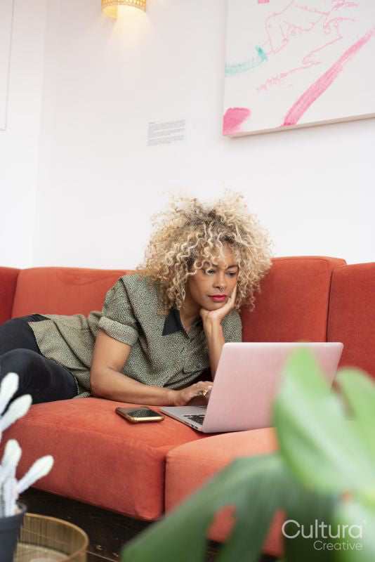 Woman reclining on sofa and working on laptop