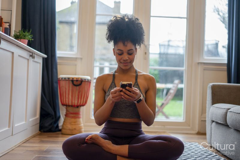 Young woman doing yoga and using phone at home