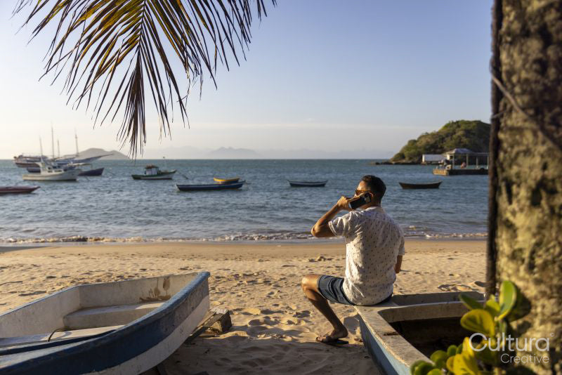 Rear view of man sitting at beach talking on phone