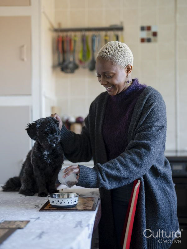 Portrait of woman pouring dog food into bowl in dining room