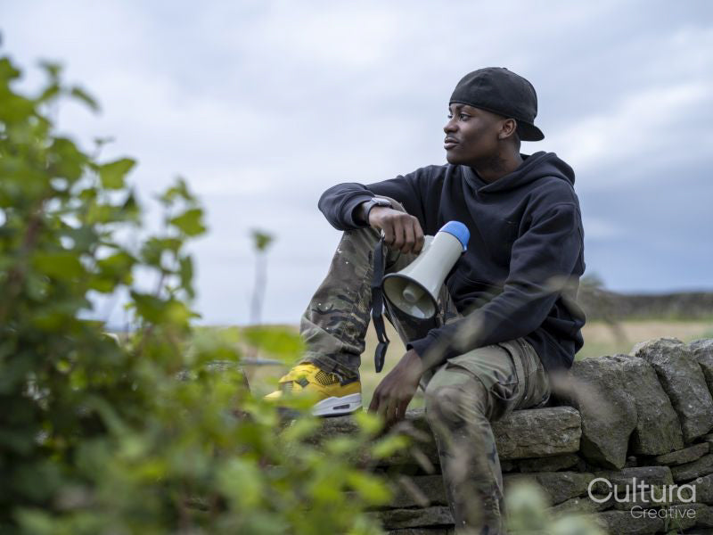 Young man sitting on stone wall holding bullhorn